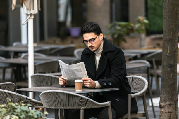 istock Smiling businessman wearing suit reading newspaper while sitting at the cafe and drinking coffee 1344013739