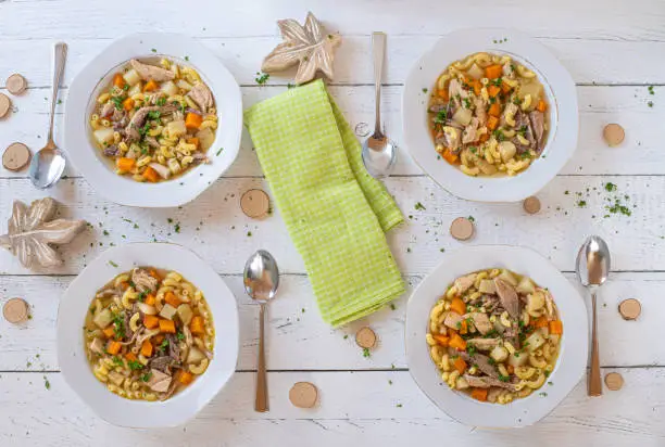 Background image of a family dinner or lunch with fresh and home cooked chicken noodle  soup. Served on 4 white plates and spoon on white wooden table.