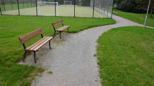 entrée à l’aire de jeux extérieure avec tapis de gazon artificiel. terrain de jeu scolaire rural dans le parc avec des bancs et des chemins de gravier dans la pelouse. homme blanc tenant un réseau d’entrée. la barrière de capture - vacant block photos et images de collection