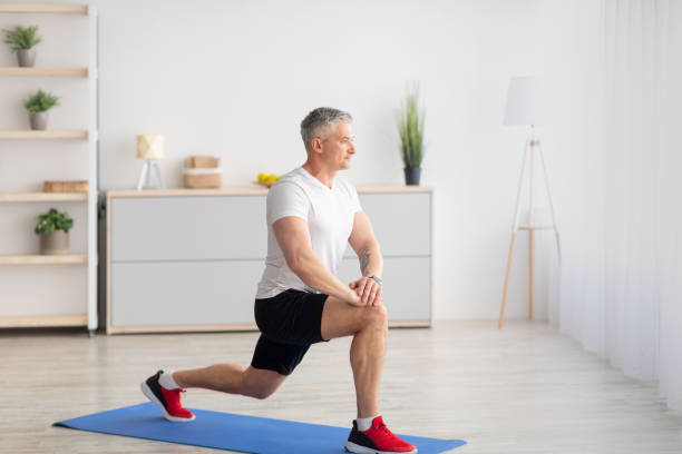 fitness en casa. hombre maduro motivado haciendo estocadas en el interior de la sala de estar, espacio libre, diseño de pancartas - lunge fotografías e imágenes de stock