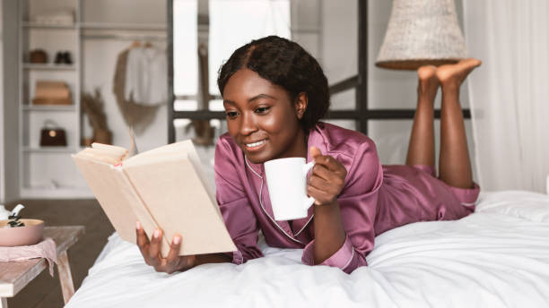 istock Black Lady Relaxing Reading Book Drinking Coffee Lying In Bedroom 1344020493