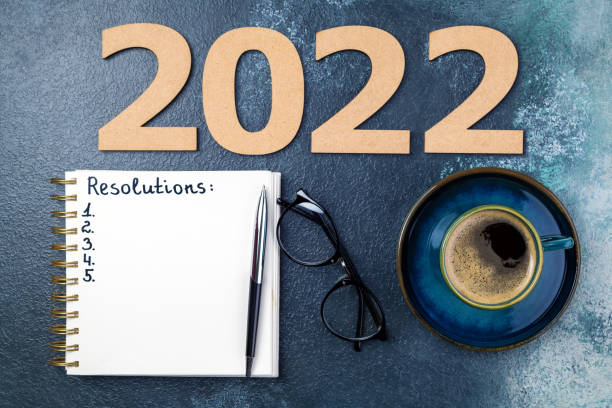 istock New year Resolutions 2022 on desk. 2022 Resolutions with open notebook, coffee cup, eyeglasses on blue background. Resolutions, goals, planning, strategy, business 1344021652