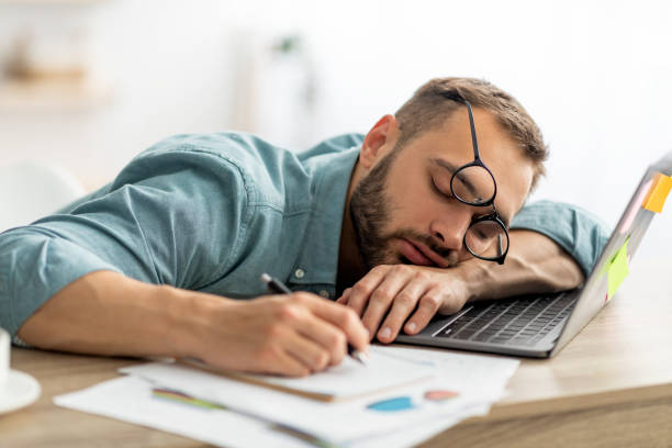 istock Exhausted millennial man sleeping on his office desk, next to laptop and documents, tired of overworking 1344024379