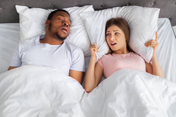 vista superior de un chico negro roncando y su novia frustrada cubriendo las orejas con almohada en la cama en casa - couple love snoring sleeping fotografías e imágenes de stock