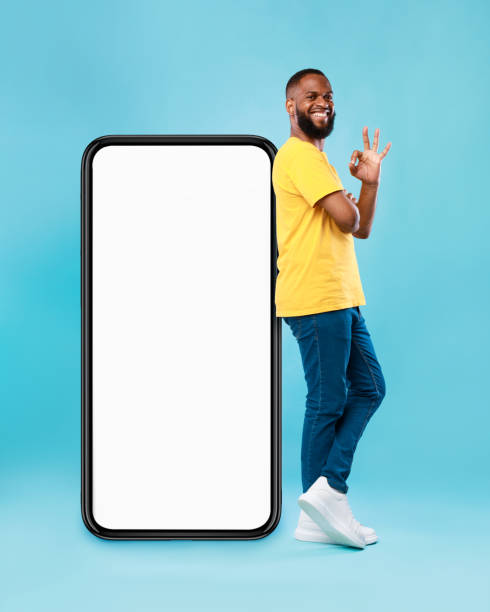 istock Optimistic black man showing ok gesture, leaning on big smarthone with blank screen, recommending new mobile app, mockup 1344027230