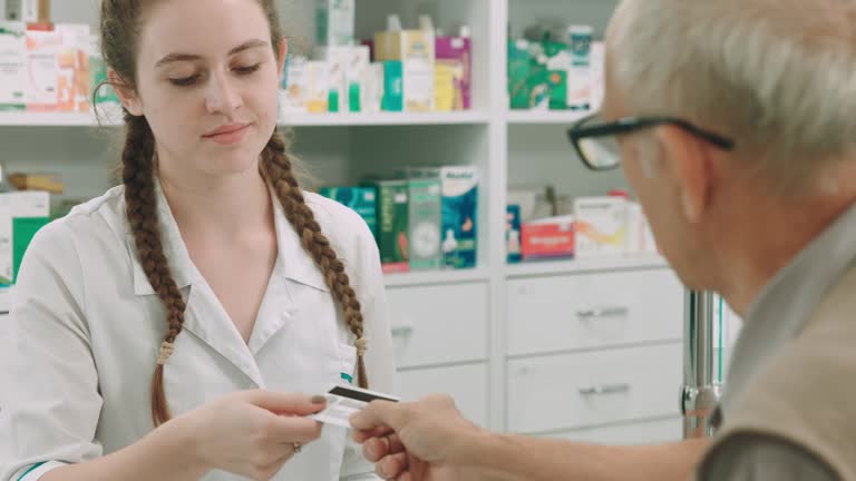 Elderly man pays at the pharmacy with the credit card to a young female pharmacist.