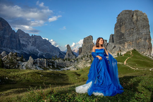 A A beautiful brunette adult princess wearing an elegant blue dress on a mountain range on a lovely summer's day