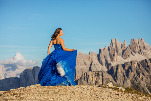 A A beautiful brunette adult princess wearing an elegant blue dress on a mountain range on a lovely summer's day