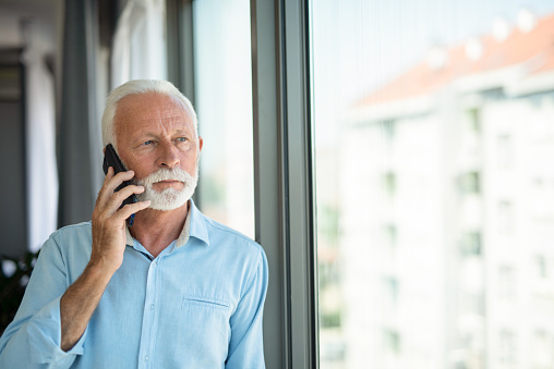 Senior businessman having a phone conversation next to window.