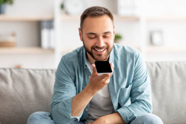 istock Cheerful millennial guy sitting on couch with cellphone at home, mockup for mobile app or website on screen 1344037349