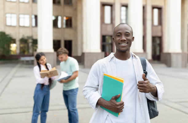 istock Happy african american student guy standing outdoors with classmates in university campus, posing and smiling to camera 1344037795