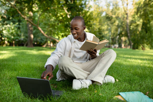 istock Preparing for exams outdoors. Happy black student guy studying with book and laptop computer, sitting in campus 1344037816