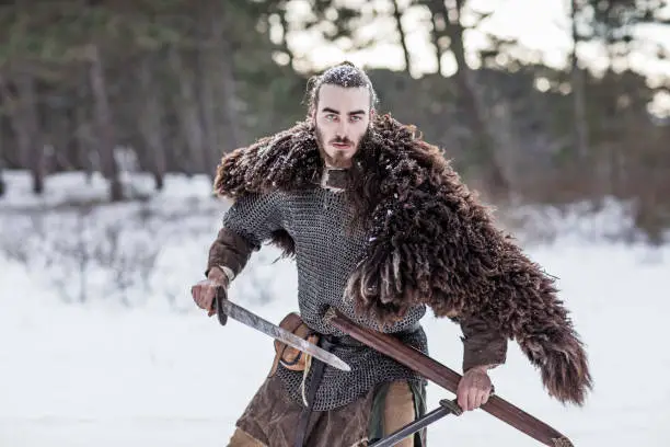 Handsome weapon wielding viking rus warrior outdoors in a snow filled wintry forest scene