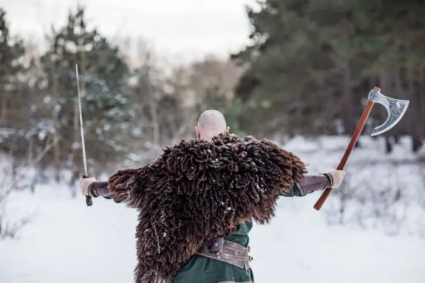 Handsome weapon wielding viking rus warrior outdoors in a snow filled wintry forest scene
