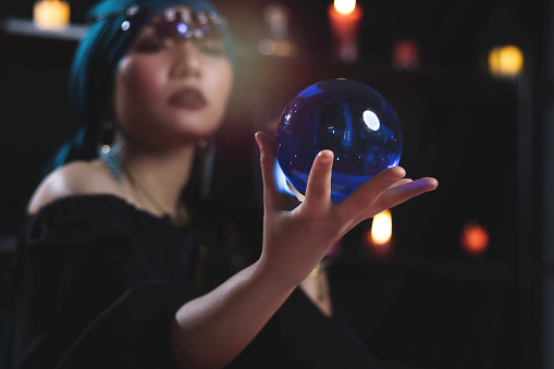Crystal ball in hand of mysterious magnificent beautiful woman fortune teller in black dress, dark witch try to read future on magical ball.