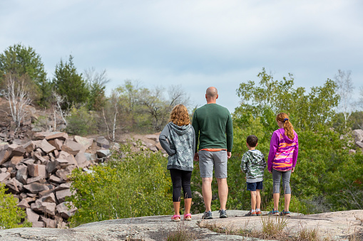 Rear view of a father and three children standing on a slab of granite at a scenic overlook at an old granite quarry. Taken on a beautiful early autumn day with the leaves just beginning to change colors.