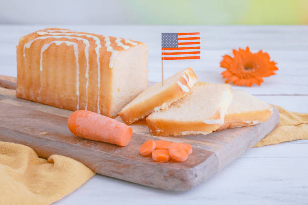 Carrot cupcake on the table A delicious cake with sugar icing, a flower, a paper American flag and fresh carrots lies on a wooden board on the table, close-up side view. Carrot cake national day concept. carrot cake day stock pictures, royalty-free photos & images