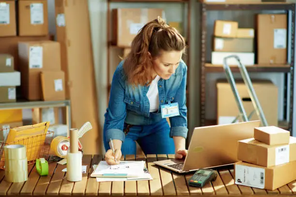 Delivery business. young female in jeans with laptop in the warehouse.