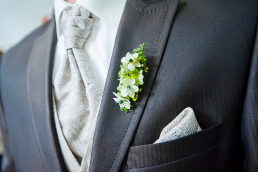 Closeup of a groom's suited chest with the focus on his buttonhole flowers.
