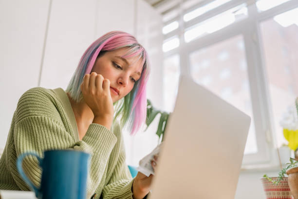istock Young woman using laptop while drinking hot drink at home 1344073797
