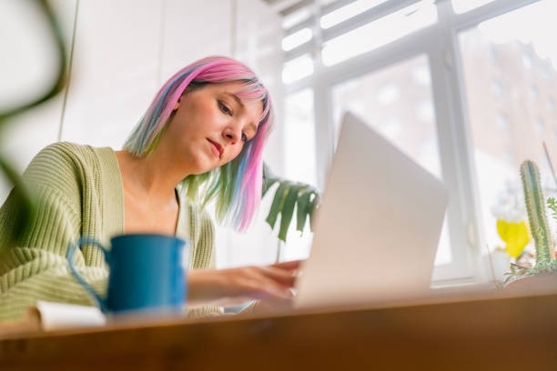 istock Young woman using laptop while drinking hot drink at home 1344074641