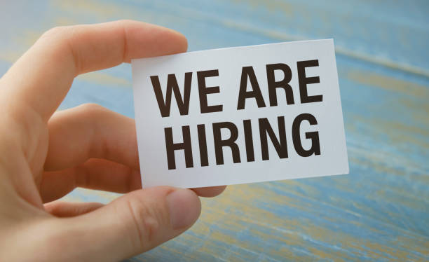 istock Hand holding placard billboard poster with text: Now Hiring, isolated on grey background. Finding a job, looking for a job concept. 1344075752