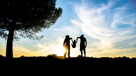 silhouette concept. young happy family on top of a hill outdoor enjoying golden hour at sunset. mom, dad and little boy swinging into the air holding parents hands. freedom, youth, love and lifestyle