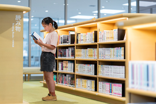 Young girl reading a book in a library. Okayama, Japan