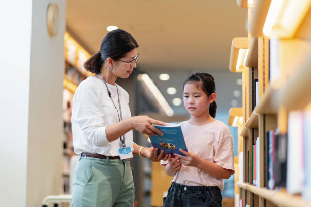 bibliothekarin hilft einem jungen mädchen bei der suche nach einem buch - librarian stock-fotos und bilder