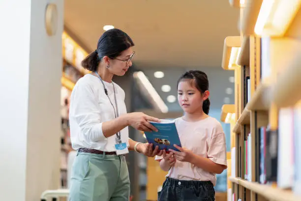 Librarian helping a young girl to search for a book. Okayama, Japan