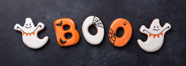 istock Horizontal banner with text BOO from gingerbread cookies and ghosts on dark stone background. Halloween concept 1344083179