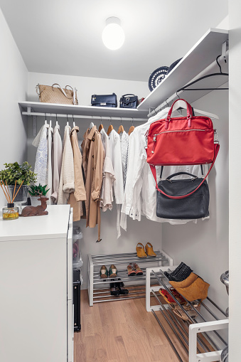 A walk-in closet with various jackets, shirts, bags and shoes and a dresser.