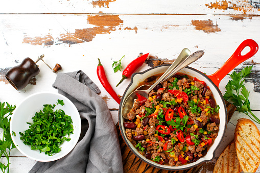 Traditional Mexican food - Chili con carne with minced meat and vegetables stew in tomato sauce in a cast iron pan on light gray slate or concrete background. Top view with copy space
