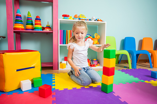 Cute little girl playing with colorful blocks at home