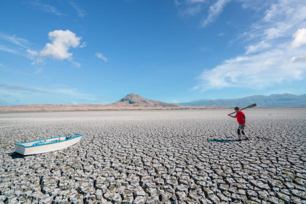 fishmerman is hopelessly going to his boat on dried cracked drought lakebed surface - backpack one mature man only only mature men one man only imagens e fotografias de stock