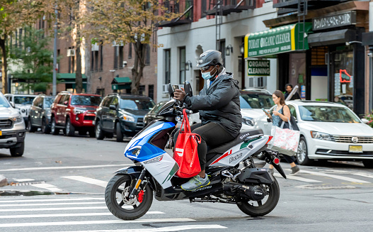 New York, NY, USA - September 28, 2021: Delivery man reads his phone as he rides south on Lexington Avenue.