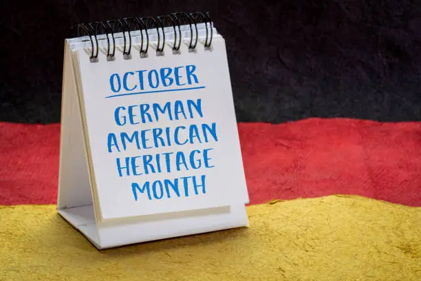 October - German American Heritage Month, handwriting in a small desktop calendar against paper abstract in colors of Germany national flag, reminder of cultural event