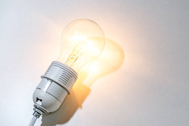 istock Light bulb turned on, on white surface. Shadow of the light bulb. 1344090076