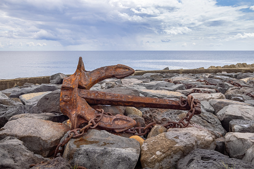Anchor at stony ground used as a decoration at the harbor in the village Povoacao on the south coast of the Portuguese Azorean Island San Miguel in the middle of the North Atlantic Ocean