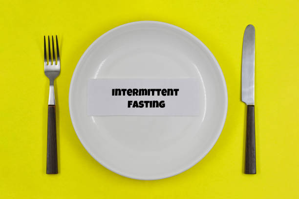 istock Table setting, empty white plate with fork and knife on yellow background, with one of the principles of healthy living - Intermittent fasting 1344094435