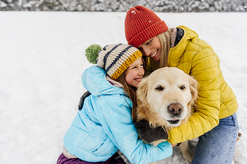 Photo of smiling girl and her mother on snow,  enjoying with their dog