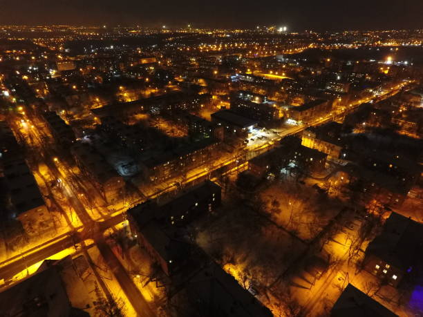 Night city in snow and lights. There is a moon and clouds in the sky. Snow-covered streets with yellow-spotted lanterns. Mariupol Night city in snow and lights. There is a moon and clouds in the sky. Snow-covered streets with yellow-spotted lanterns mariupol stock pictures, royalty-free photos & images