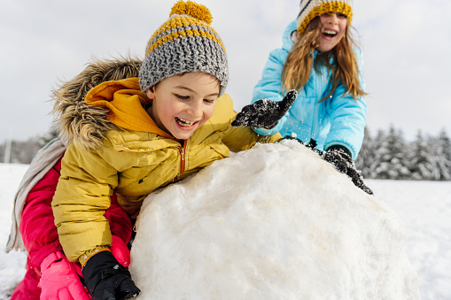 Photo of kids having fun outdoors on a winter day, building a snowman