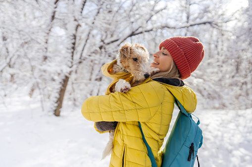 Photo of young woman and her little dog enjoying in the forest on a snowy day