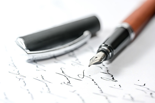 Nostalgic fountain pen and cap on an illegible handwritten letter or manuscript, close-up with selected focus and narrow depth of field