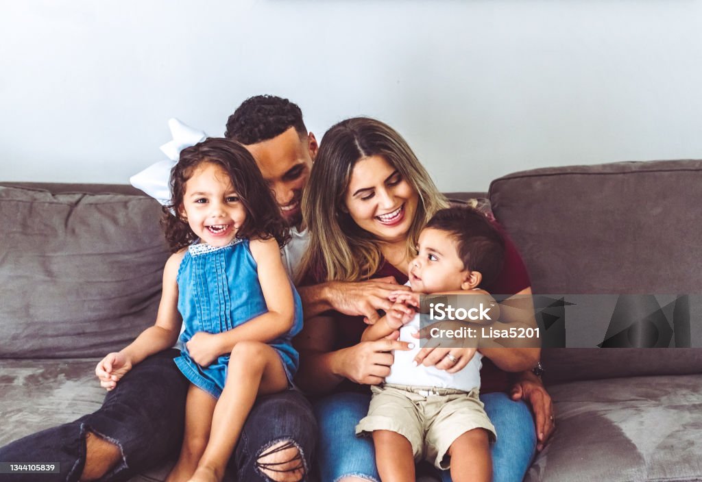 Happy multiracial family at home with two young children in casual portrait on their couch Cute family in their living room, at home portrait Family At Home Stock Photo