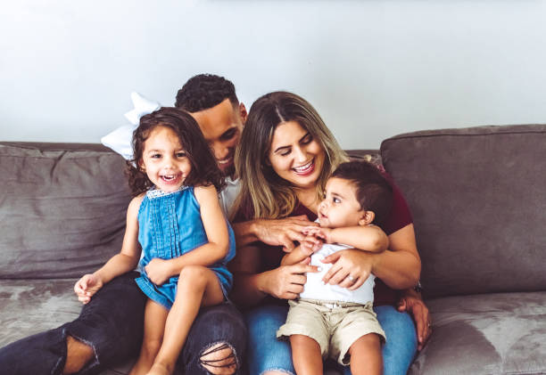 família multirracial feliz em casa com duas crianças pequenas em retrato casual em seu sofá - young family family portrait child - fotografias e filmes do acervo