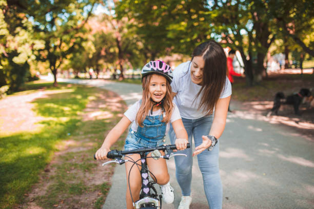 madre enseña a su hija a andar en bicicleta por el parque - helmet bicycle little girls child fotografías e imágenes de stock