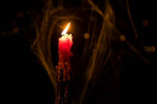 Close-up of Candle Burning and Spider Web in Background.