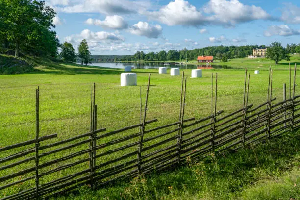 Small settlement farm in sourthern Sweden on a beautiful sunny summer day. Holiday in Swedish countryside. Vintage fence and white heystacks